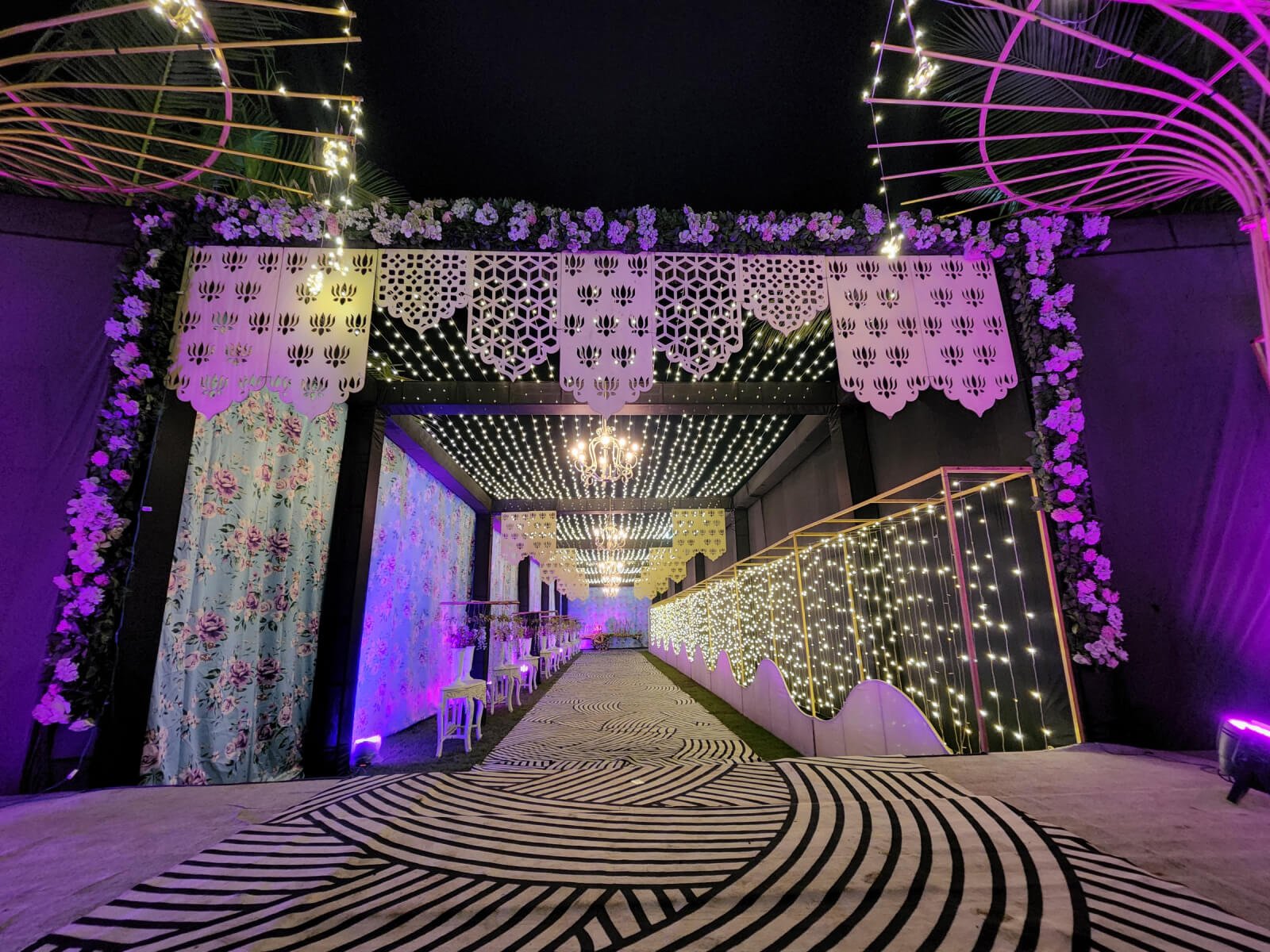 Indoor event Entrance corridor with floral decorations, hanging lights, and patterned walkway, ideal for wedding receptions and special celebrations.