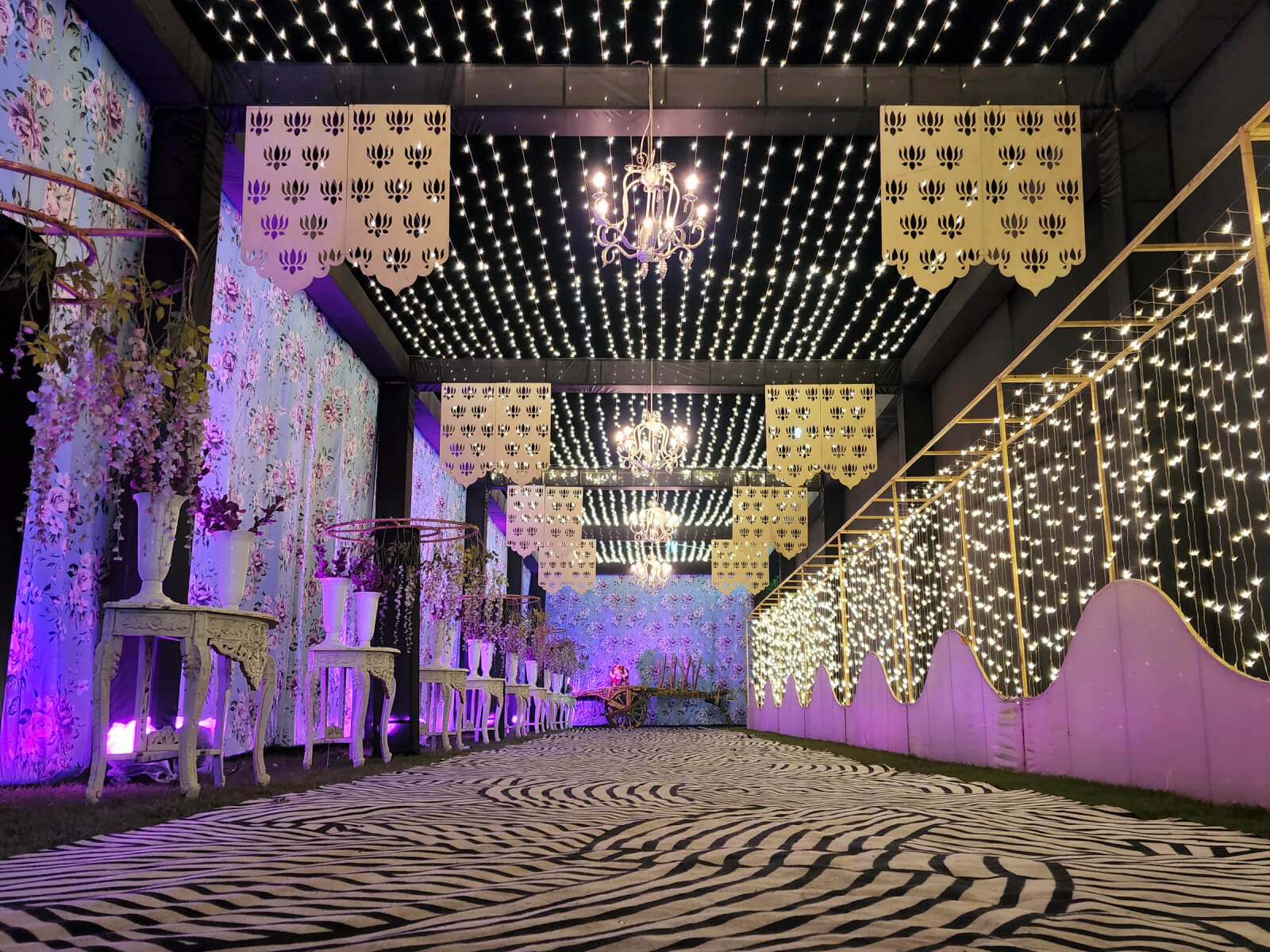 Indoor event corridor with floral decorations, hanging lights, and patterned walkway, ideal for wedding receptions and special celebrations.