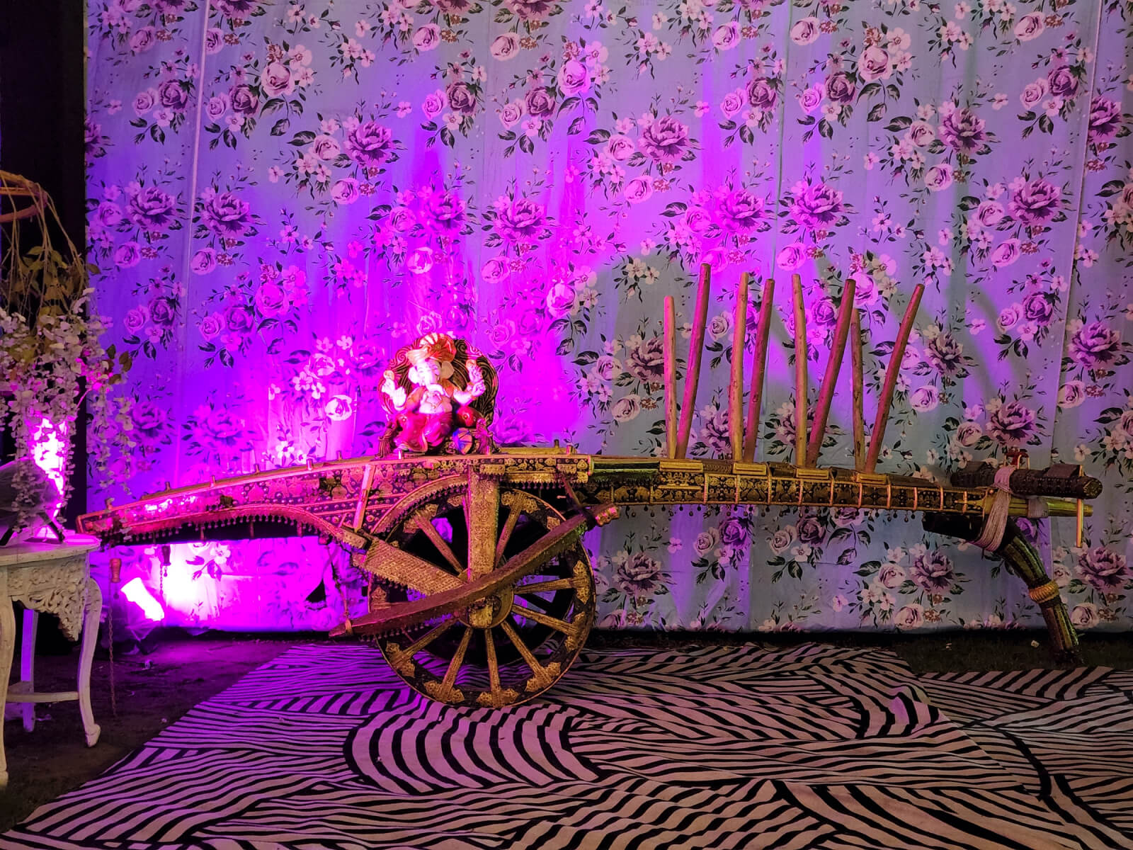 Indoor event decoration with Ganesha idol on a decorative cart, illuminated with vibrant lighting, ideal for wedding and special event setups.