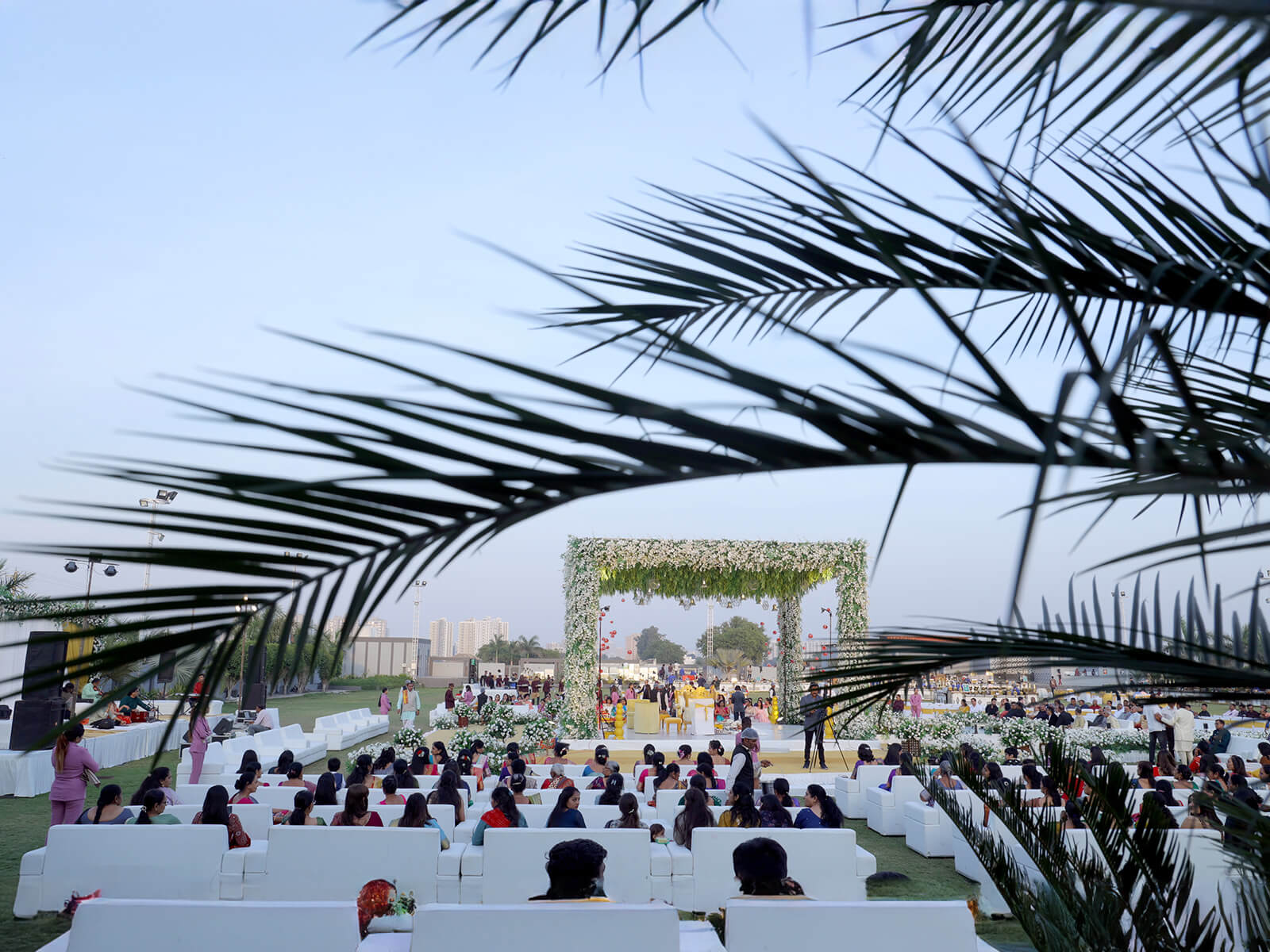 Outdoor wedding ceremony with guests seated on white chairs facing a floral arch decorated with white and green flowers.