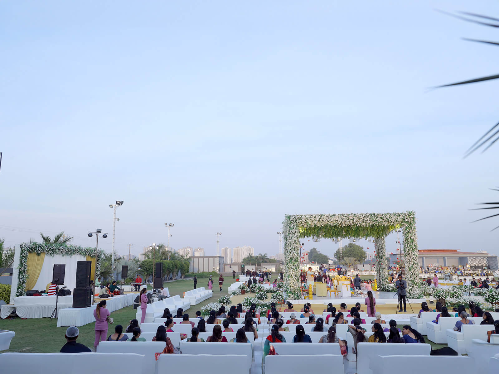 Outdoor wedding ceremony with guests seated on white chairs facing a floral arch decorated with white and green flowers.