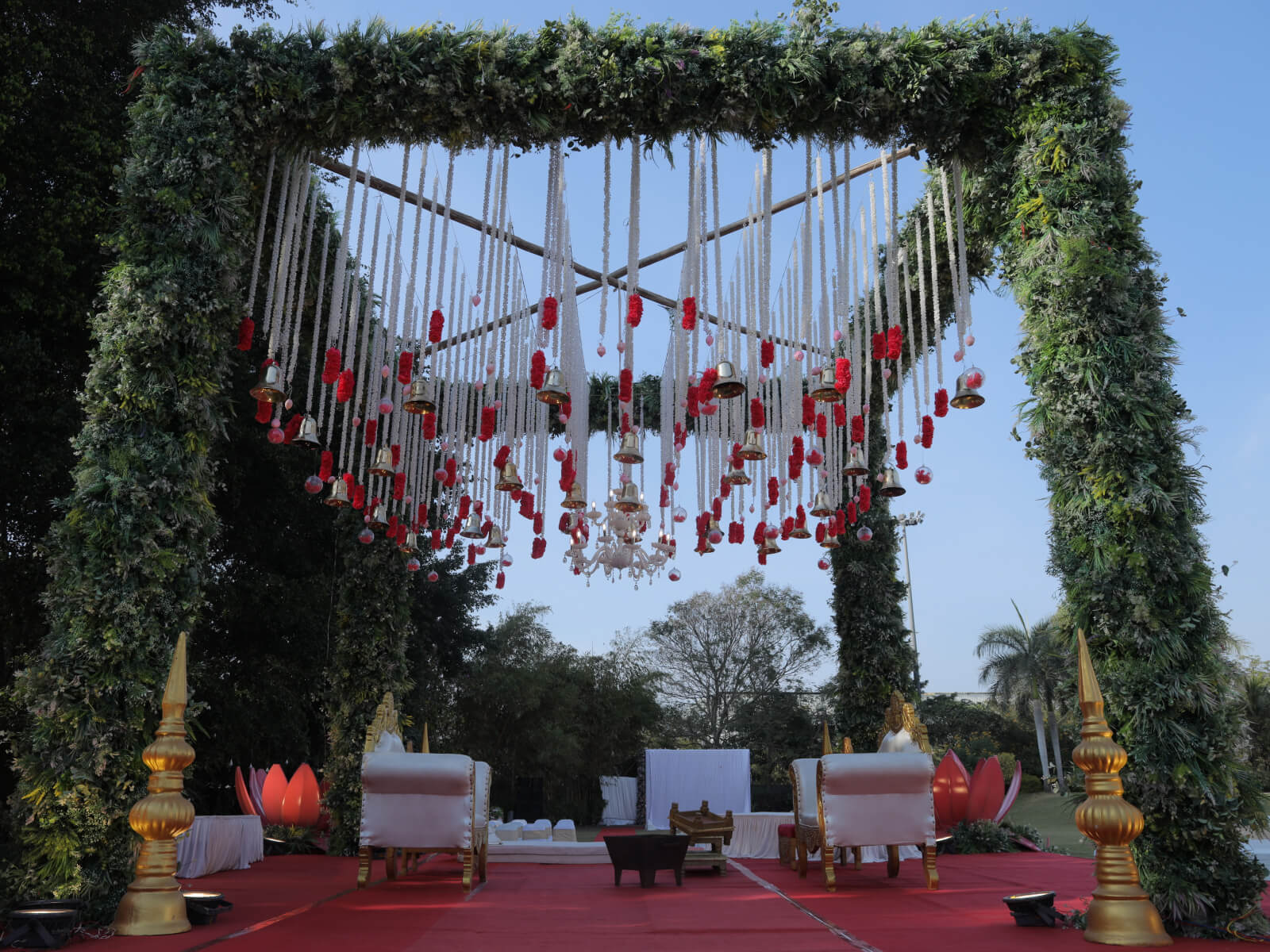 Outdoor wedding stage decorated with greenery, hanging flowers, and red garlands.