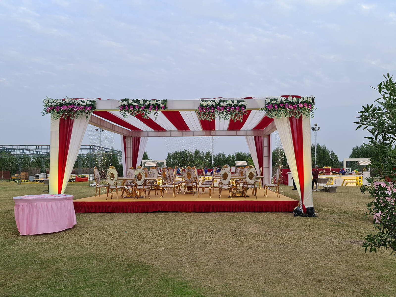 Outdoor event canopy with red and white drapes, floral decorations, and elegant seating arrangement, ideal for wedding ceremonies and special celebrations.