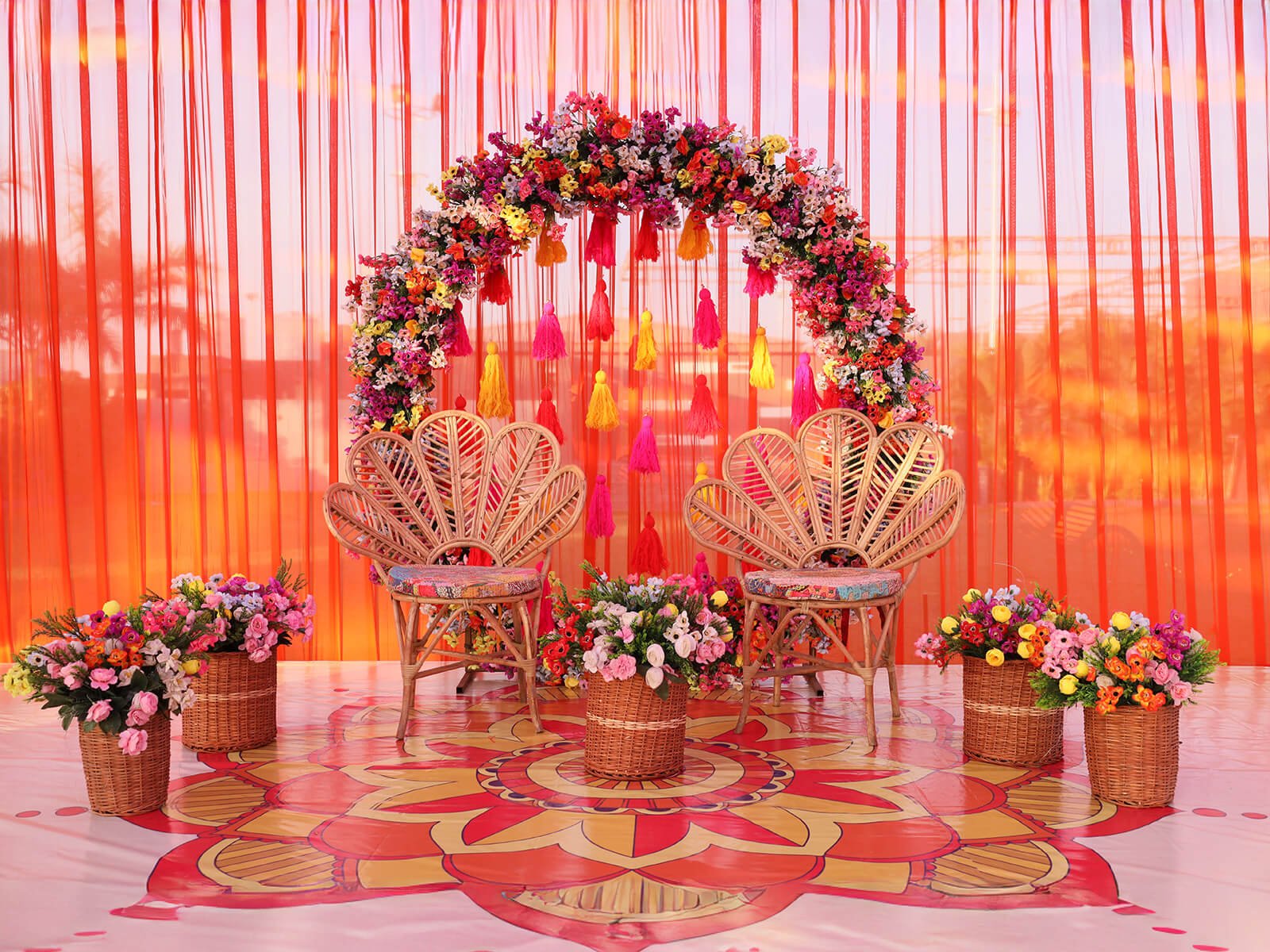 Outdoor event setup with vibrant floral arch, wicker chairs, and colorful decorations, perfect for wedding ceremonies and festive celebrations.