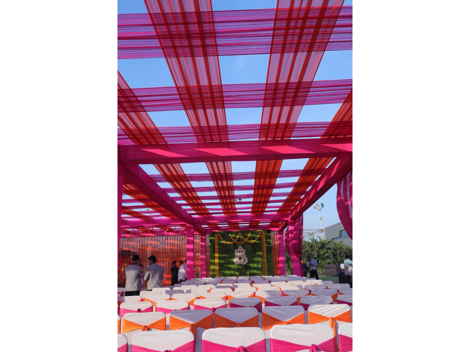 Outdoor event setup with vibrant pink and orange drapes, and decorated seating arrangement, ideal for wedding ceremonies and festive celebrations.