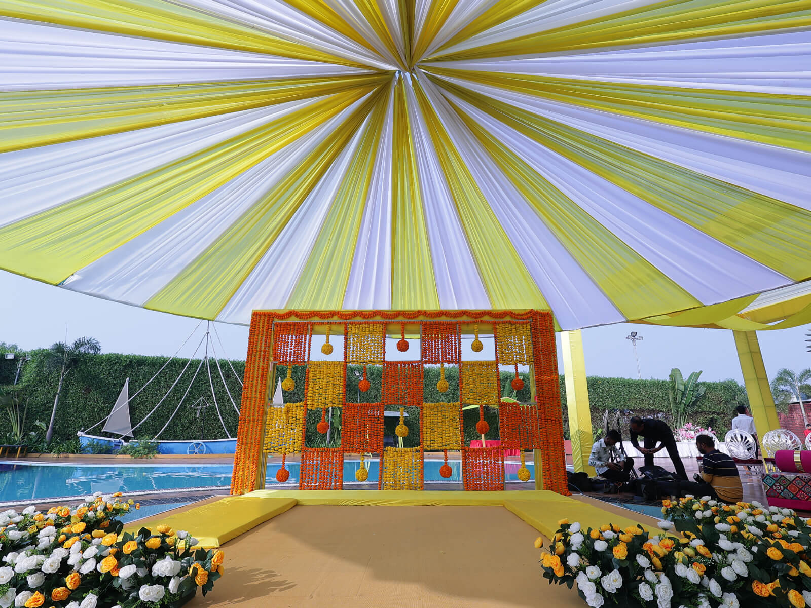 Outdoor Haldi event decoration with colorful drapes, vibrant floral arrangements, and traditional seating, ideal for wedding celebrations and event planning.