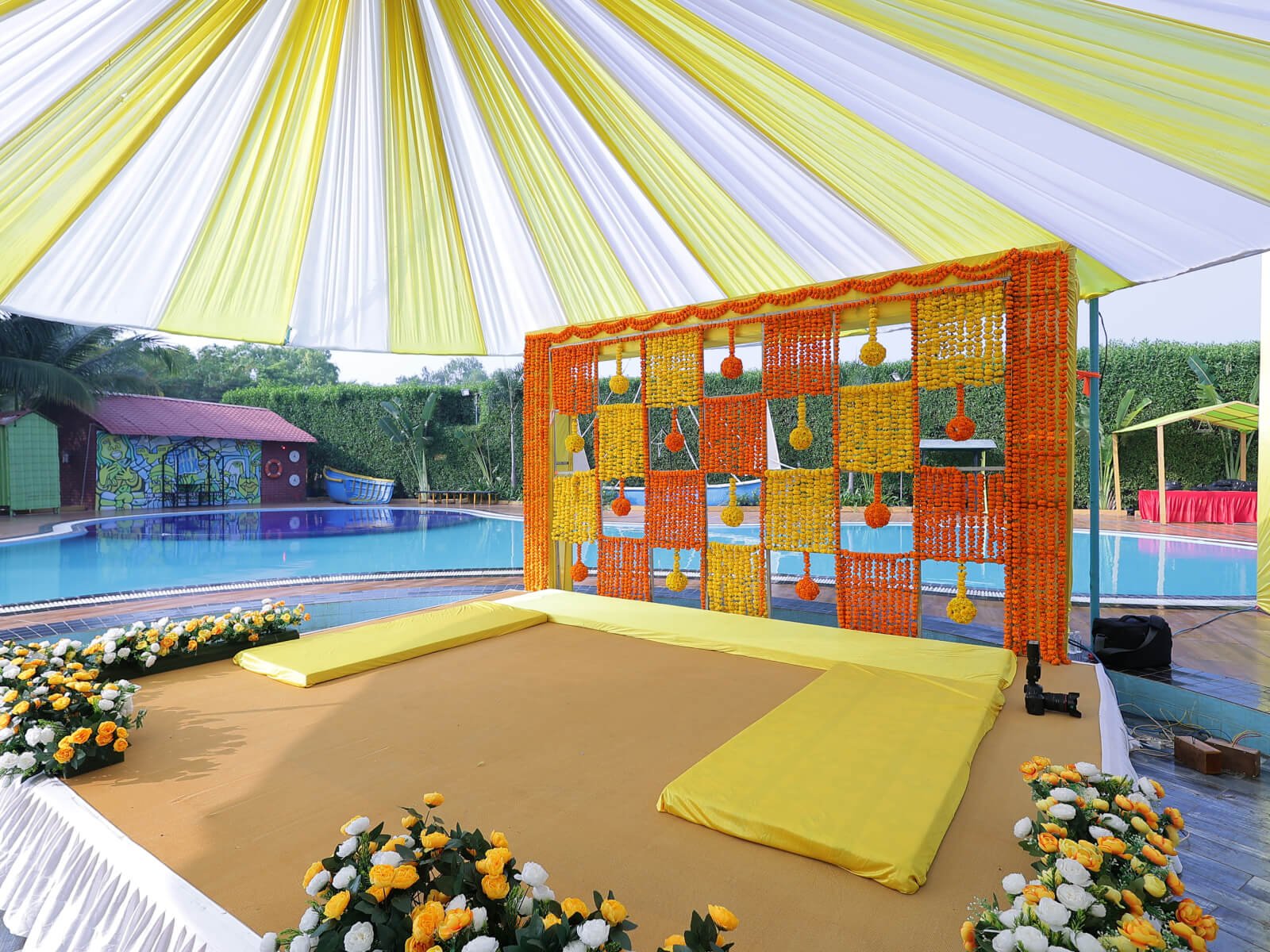 Outdoor Haldi event decoration with bright yellow drapes, floral arrangements, and traditional seating, perfect for wedding celebrations and event planning.