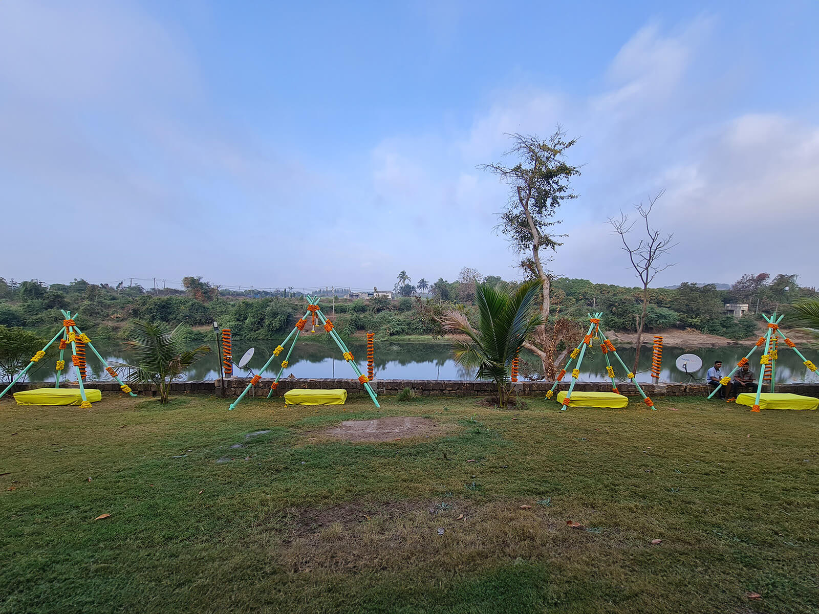 Outdoor haldi ceremony setup with decorative canopies and floral garlands by the riverside.