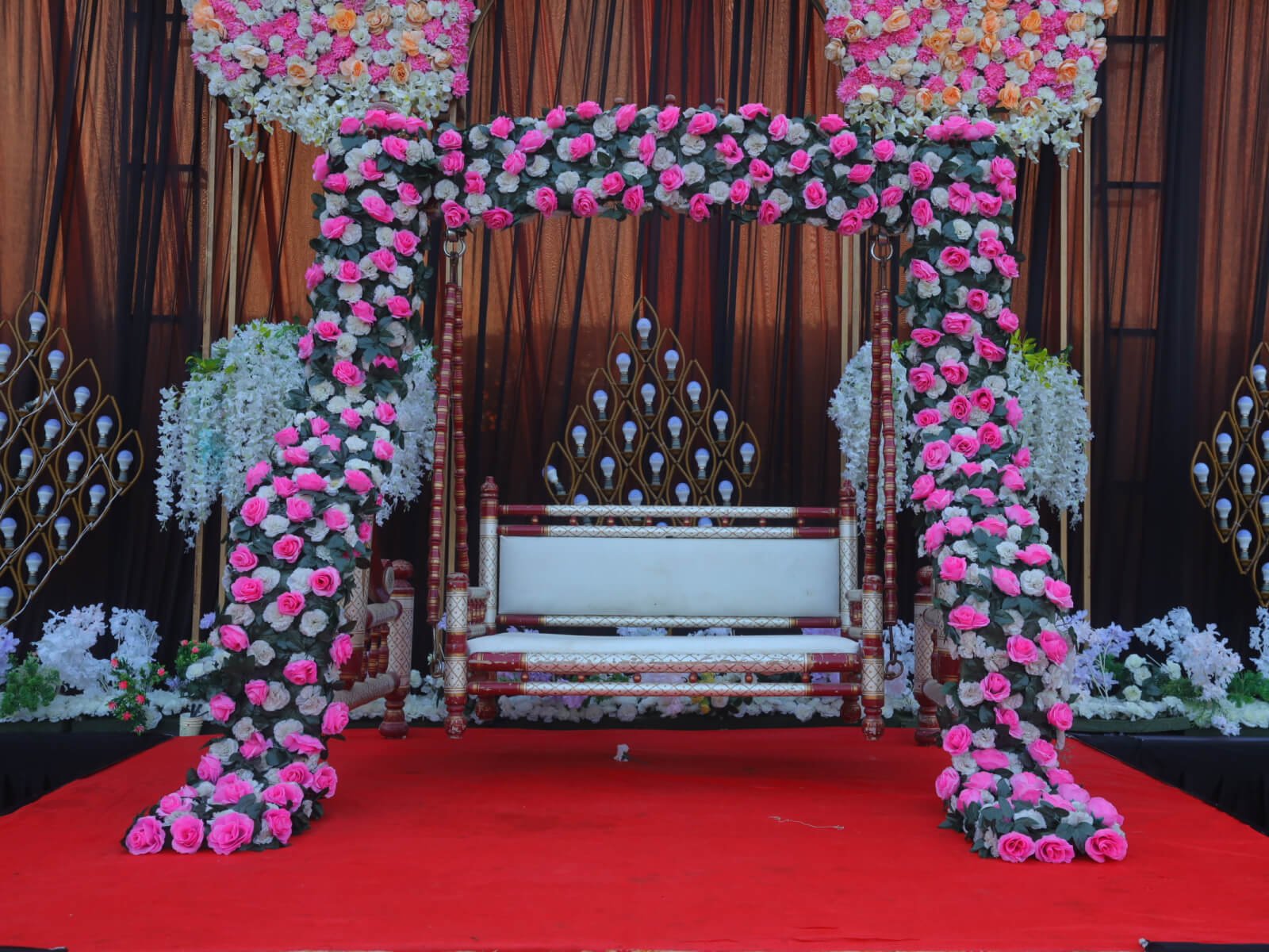 Outdoor wedding stage with a swing adorned with pink and white floral decorations, perfect for wedding ceremonies and special events.