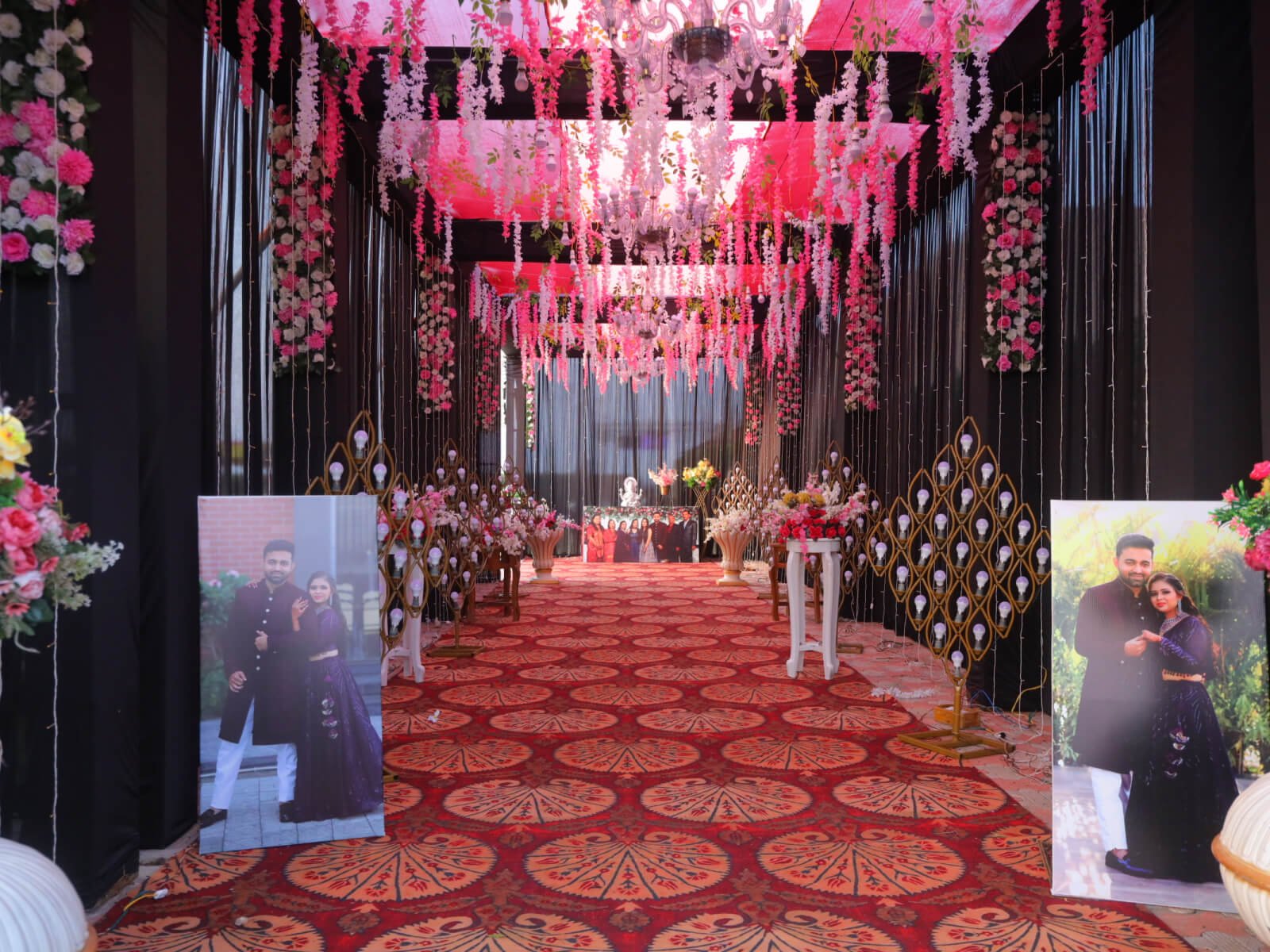 Indoor event hallway with floral decorations, chandeliers, and couple portraits, ideal for wedding receptions and romantic celebrations.