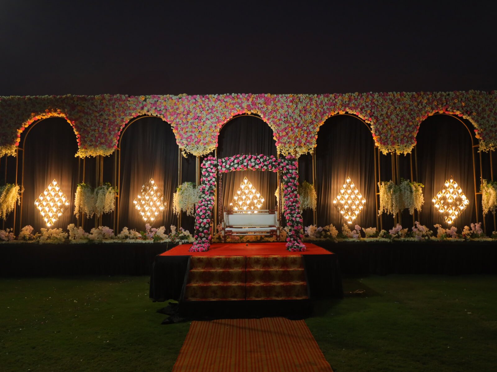 Outdoor wedding stage with floral arches and illuminated backdrop, perfect for evening wedding ceremonies and special celebrations.