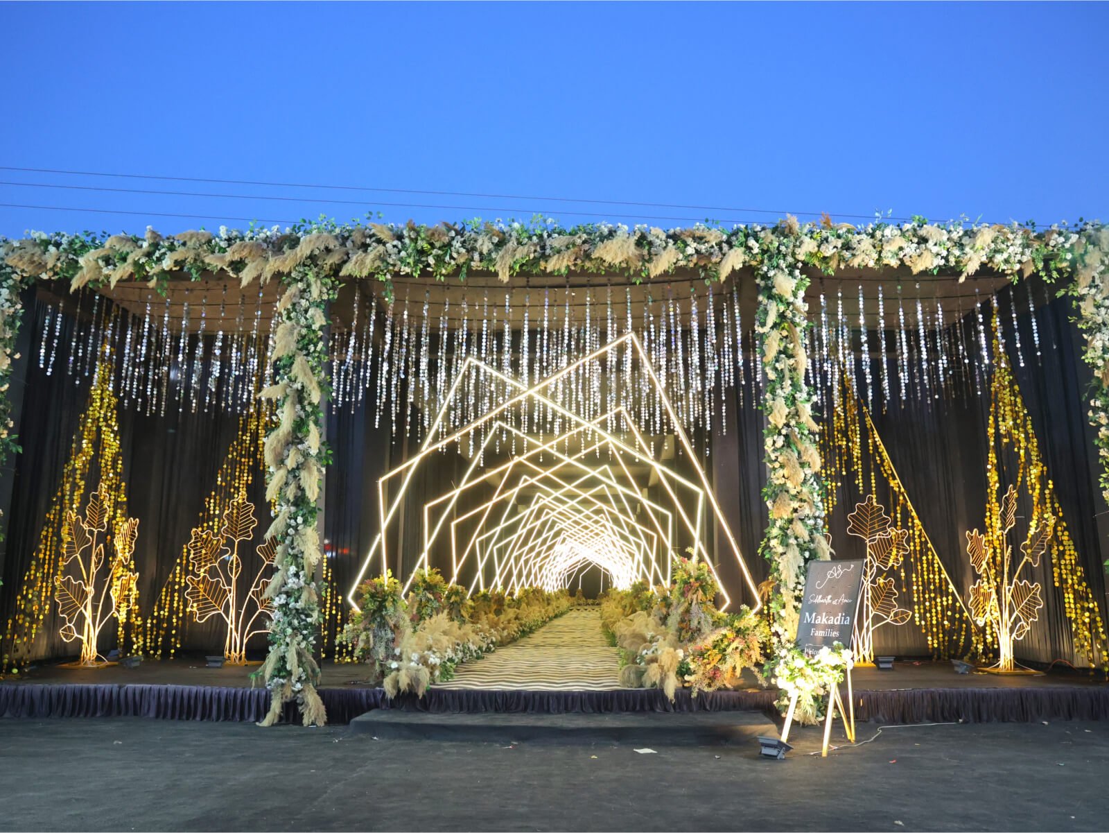 Indoor sangeet event decoration with colorful drapes, floral arrangements, and vibrant lighting, ideal for wedding celebrations and event planning.