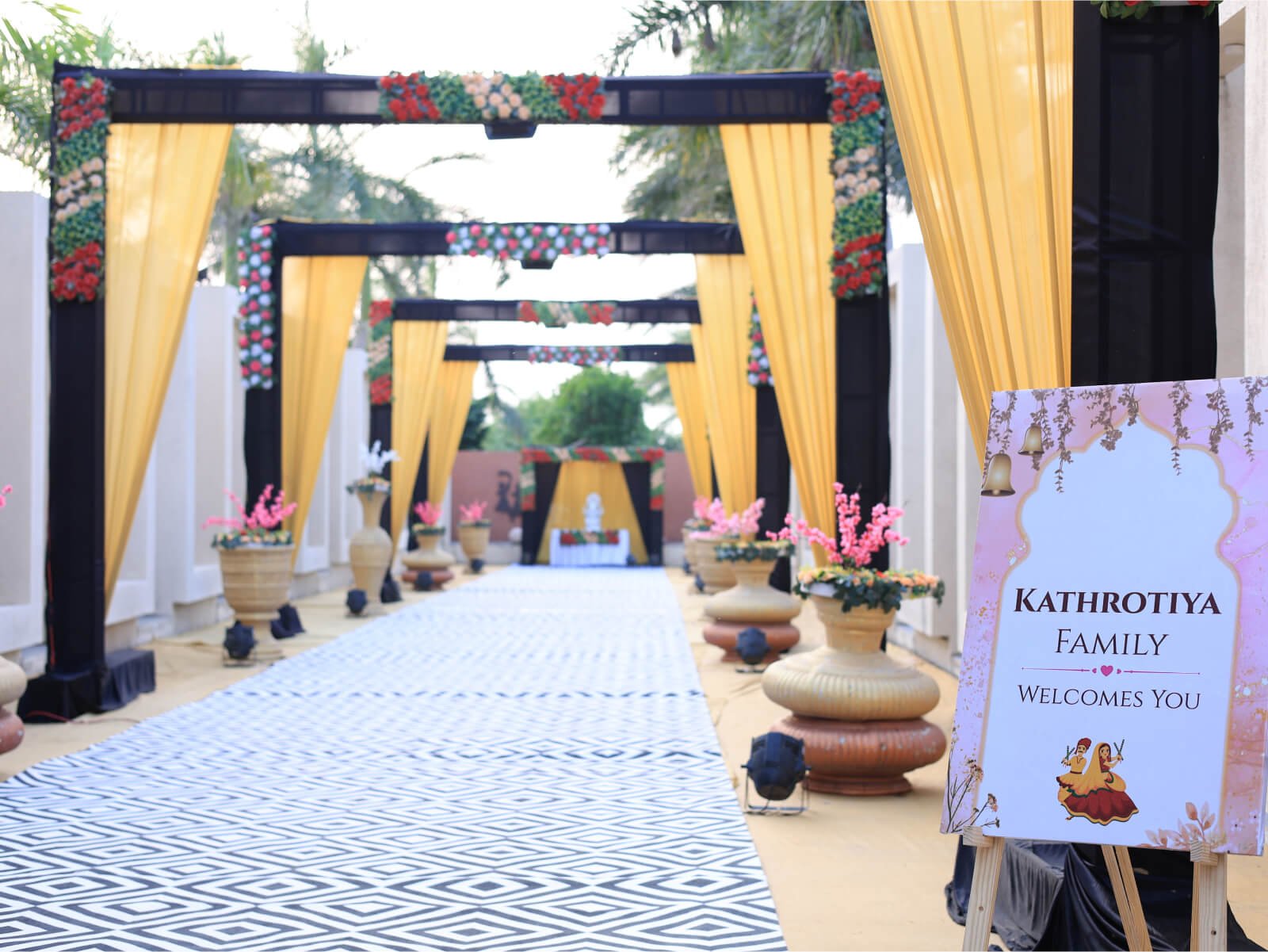 Outdoor wedding entrance with floral decorations, drapes, and a welcome sign.