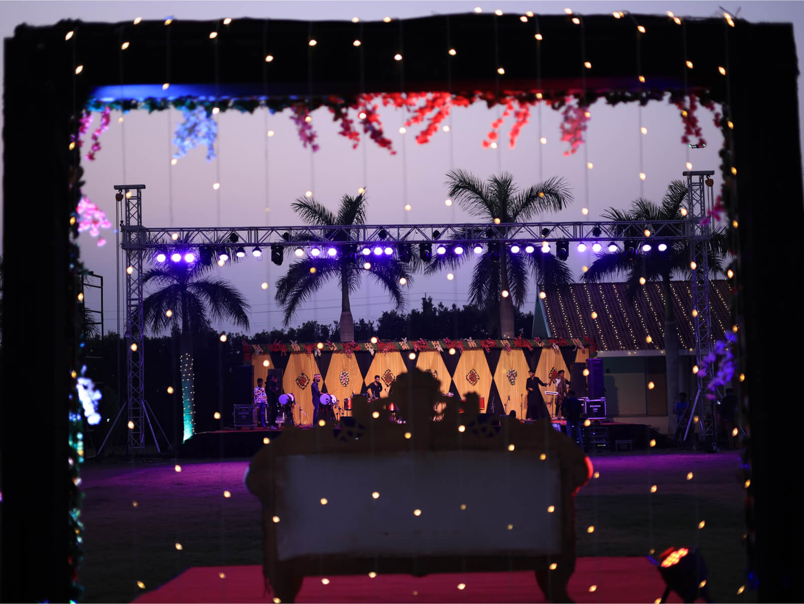 Outdoor wedding sangeet event with stage lighting and floral decorations.