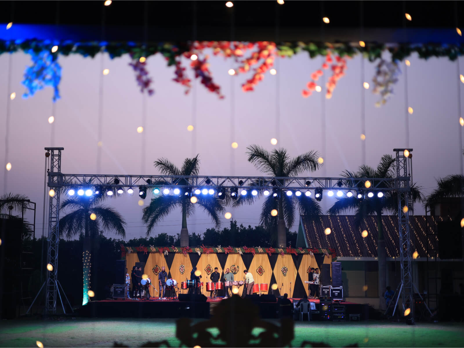 Outdoor wedding sangeet event with stage lighting and floral decorations.