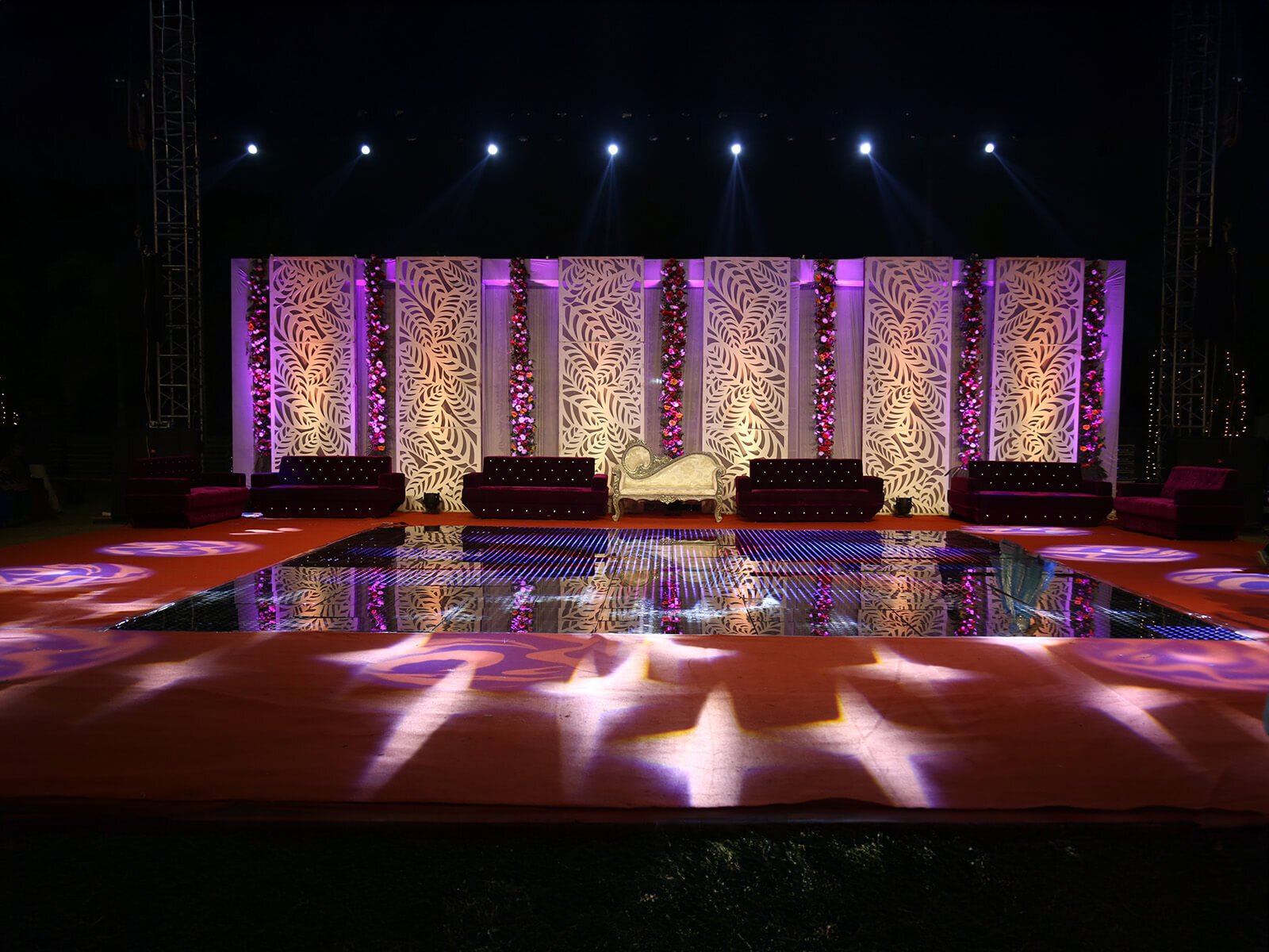 Outdoor wedding event stage with elegant floral backdrop and seating arrangement, ideal for wedding decoration, event planning, and sangeet ceremonies.