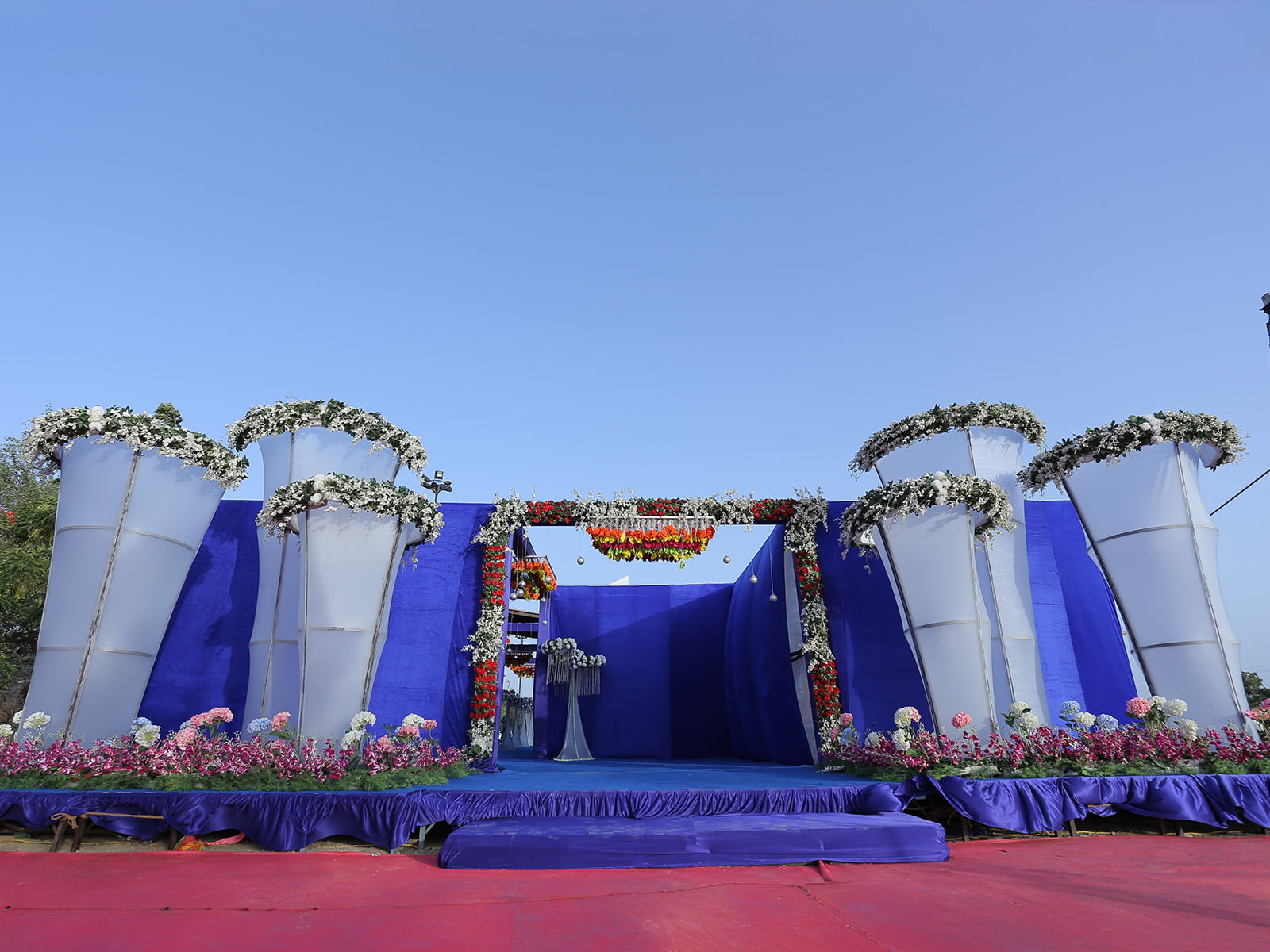 Outdoor wedding event entrance with colorful hanging decorations and floral arrangements, ideal for wedding decoration, event planning, and destination weddings.