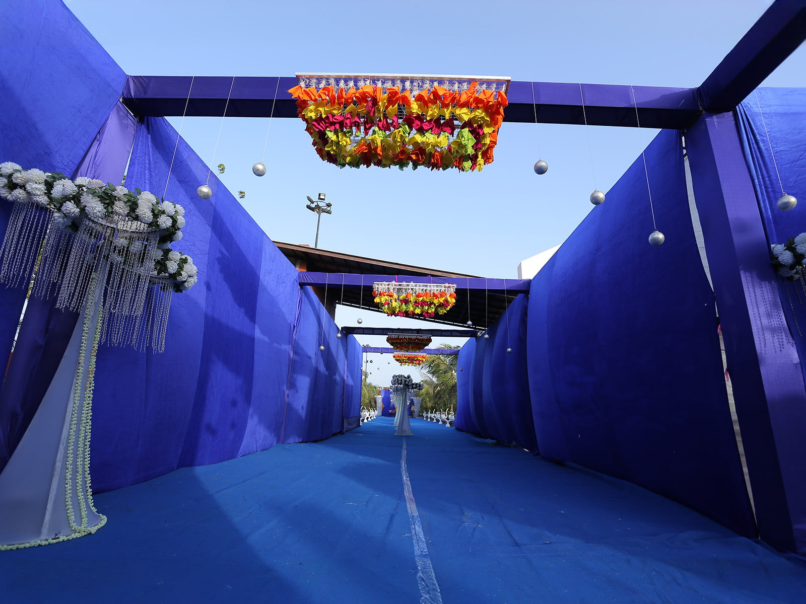 Outdoor wedding event entrance with colorful hanging decorations and floral arrangements, ideal for wedding decoration, event planning, and destination weddings.