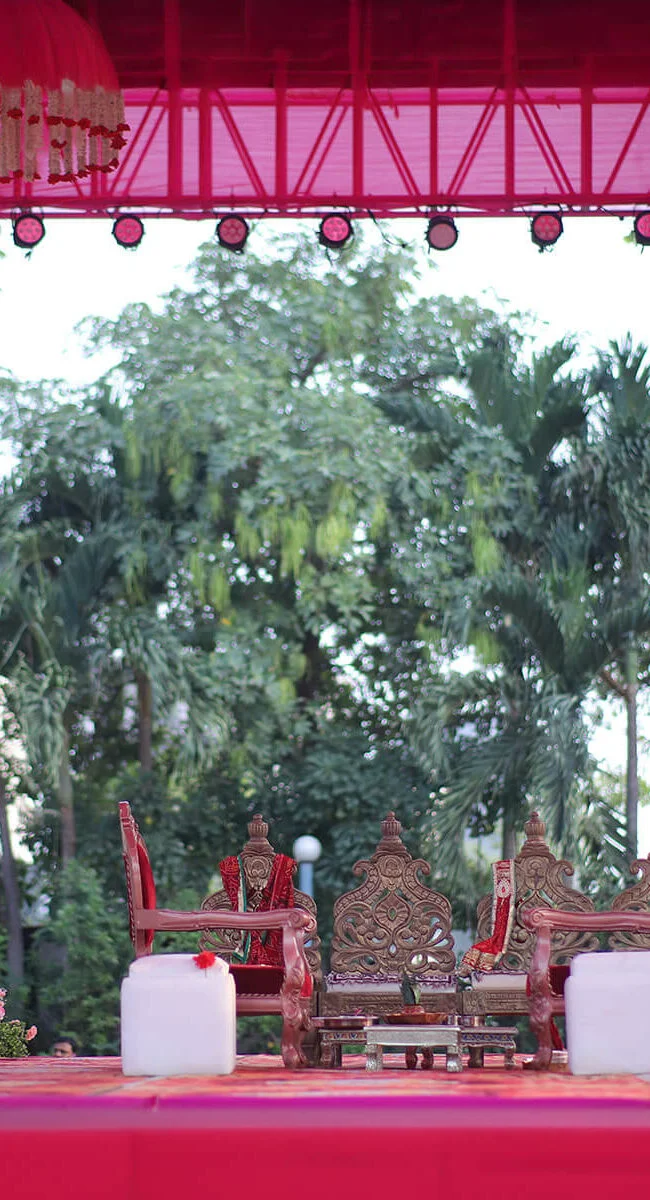 Outdoor wedding mandap with traditional chairs, floral decorations, and ceremonial setup.