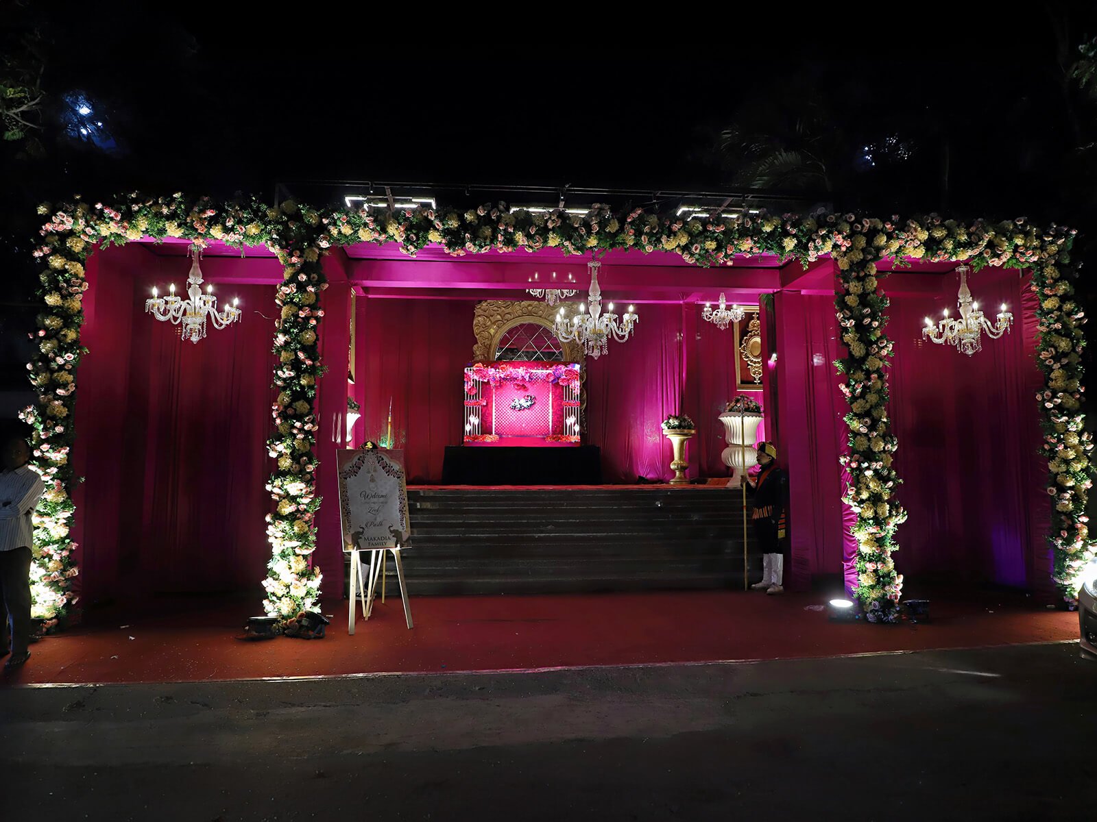 Indoor wedding entrance with vibrant drapes, floral arrangements, and elegant lighting.