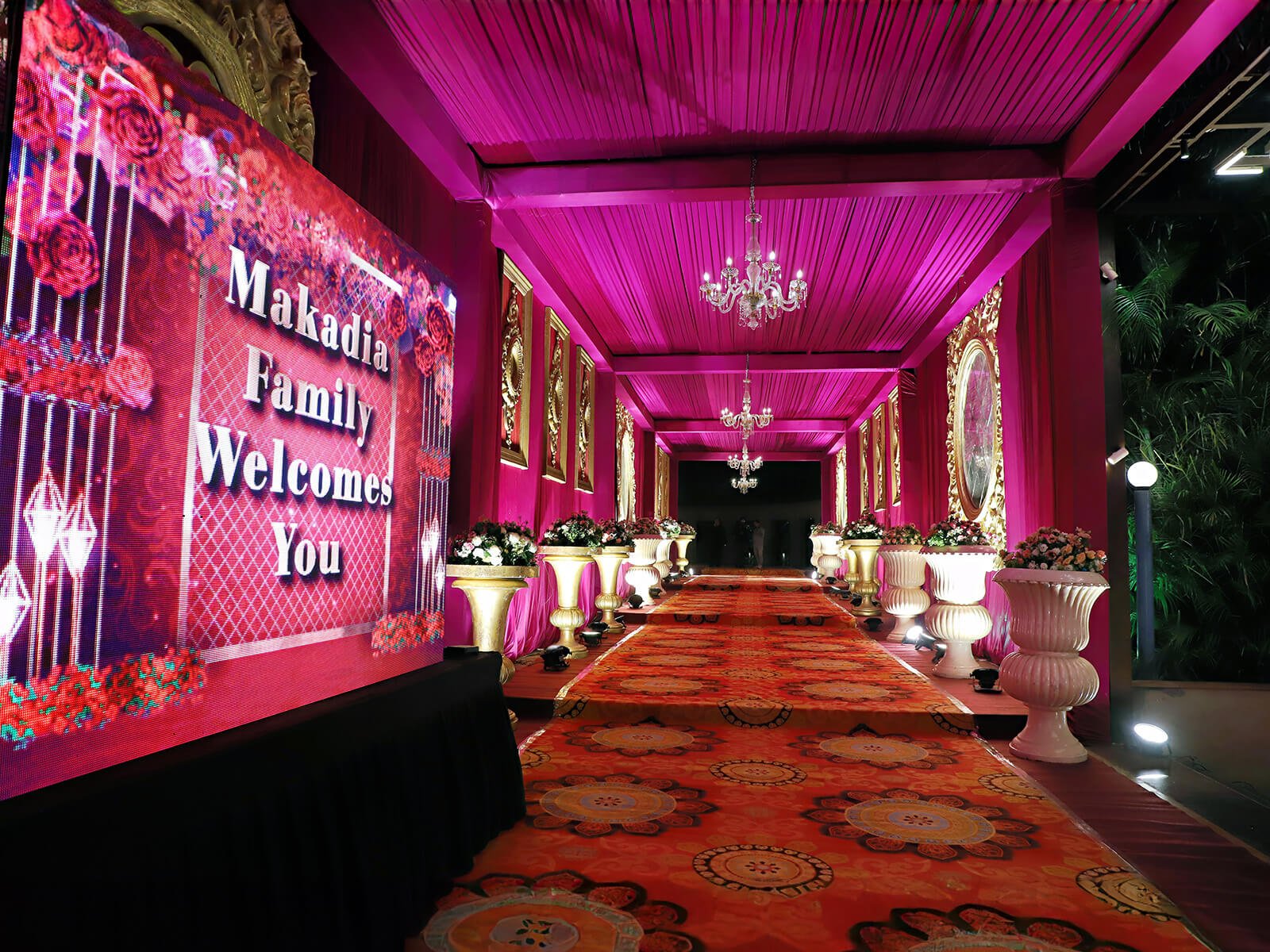 Indoor wedding entrance with vibrant drapes, floral arrangements, and elegant lighting.