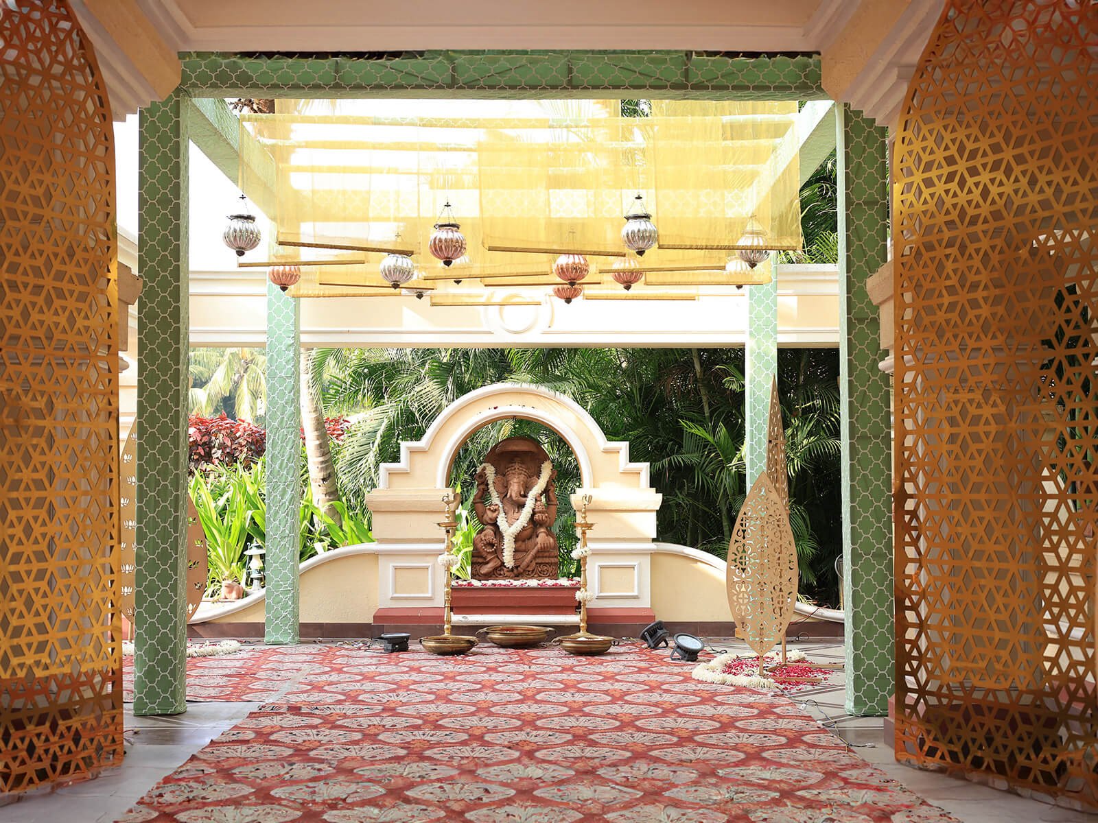 Indoor wedding decoration for a Haldi event with a Ganesha statue, ornate golden panels, and vibrant floral arrangements.