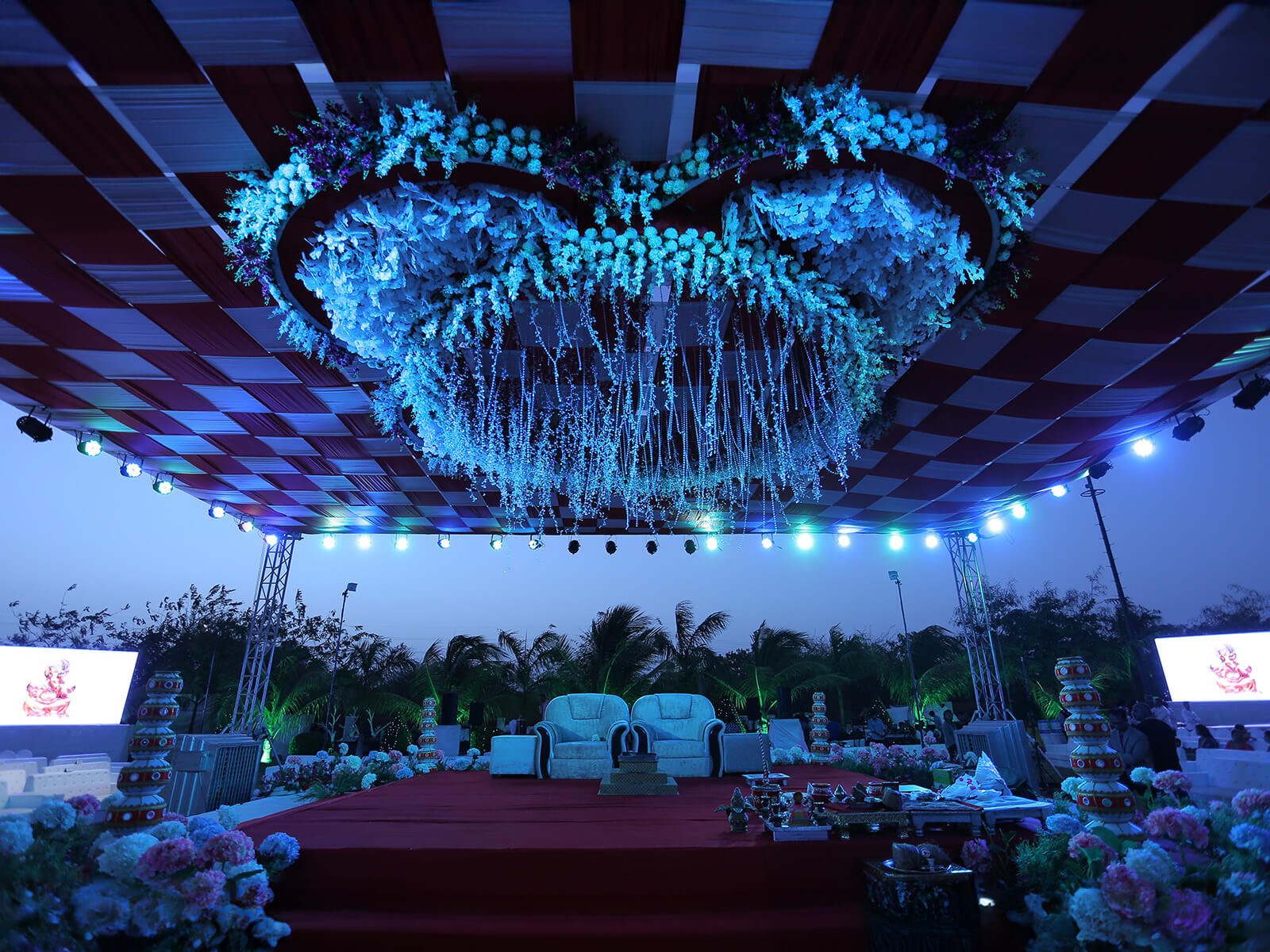 Outdoor wedding stage with vibrant lighting, floral decorations, and seating arrangements.