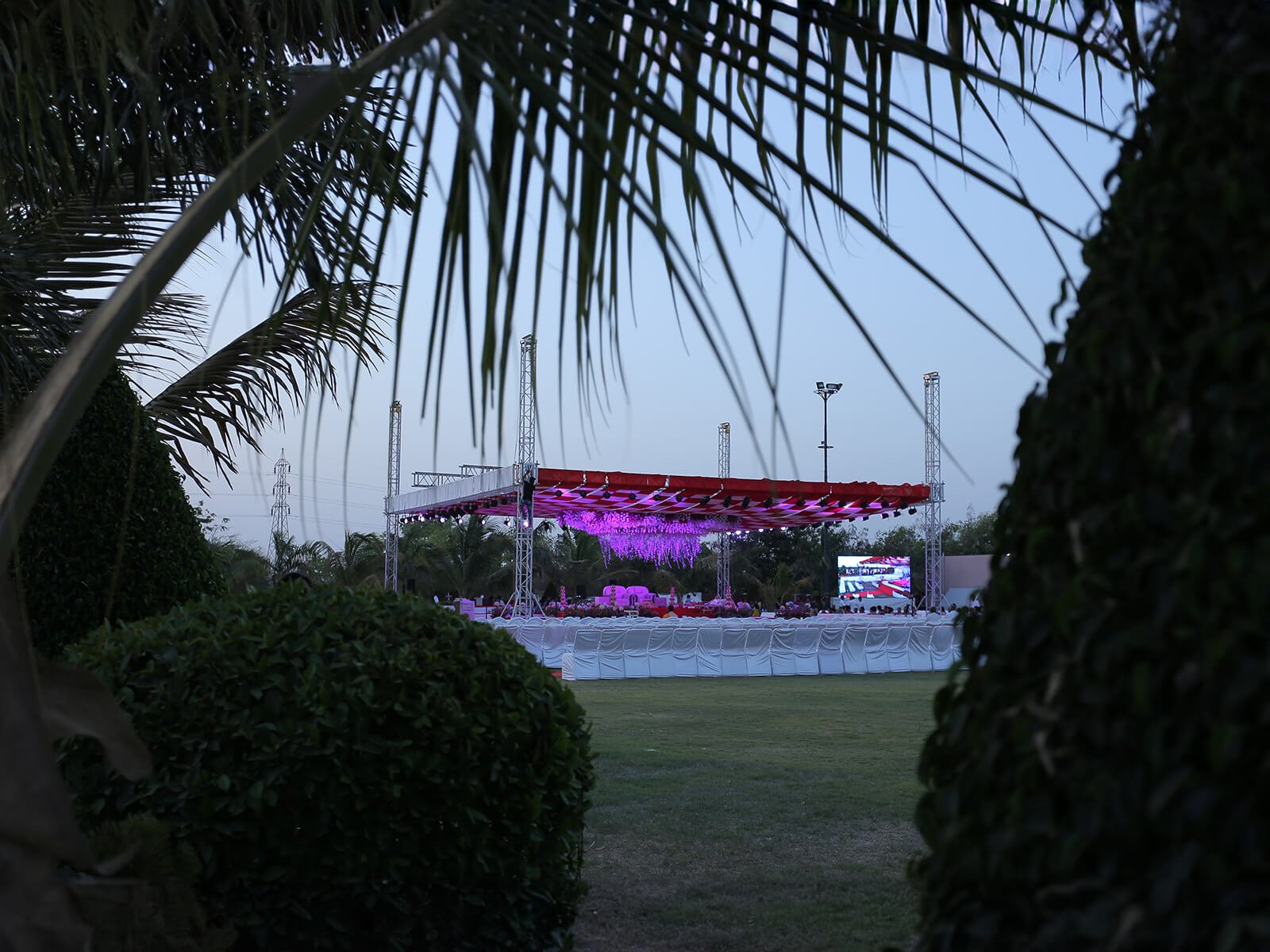 Outdoor wedding event with stage lighting and seating arrangements framed by palm trees.