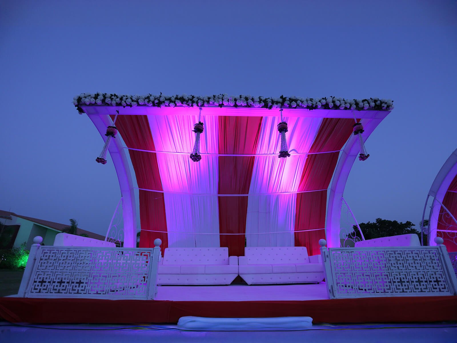 Outdoor wedding seating area with red and white drapes, floral decorations, and elegant lighting.