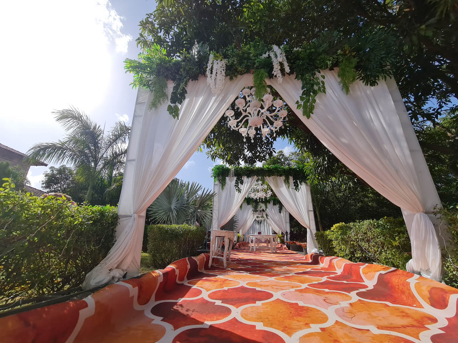 Beautifully decorated entrance with elegant white drapes and greenery, featuring a stylish chandelier and vibrant carpet, creating a grand and welcoming atmosphere for the wedding event.