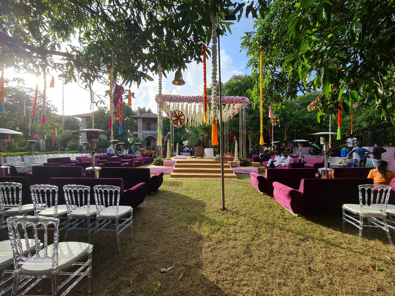 Elegant outdoor wedding setup with comfortable seating and colorful decorations under the shade of lush trees, creating a charming and intimate atmosphere for guests.